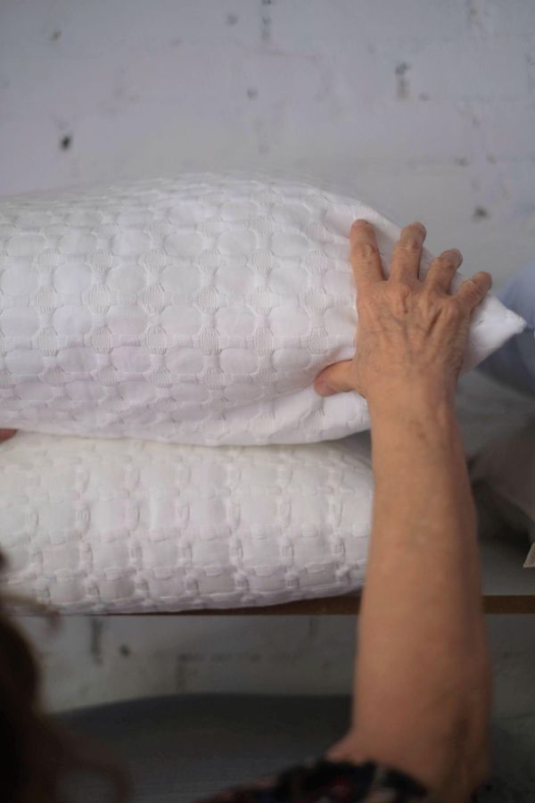 Mãos ajeitando travesseiros prontos no ateliê Le Lit